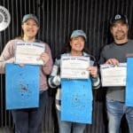 Three people holding up blue boards with a smile on their faces.