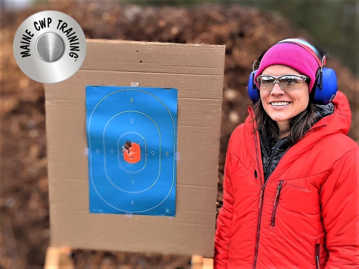 A woman standing next to a target with a rifle in front of her.