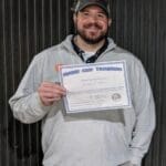 A man holding up his certificate in front of a wall.