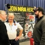 Three men are talking to each other at a gun show.