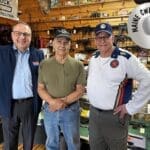 Three men standing together in a workshop with vintage equipment.