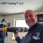 Man smiling and holding a large tool in a training room.