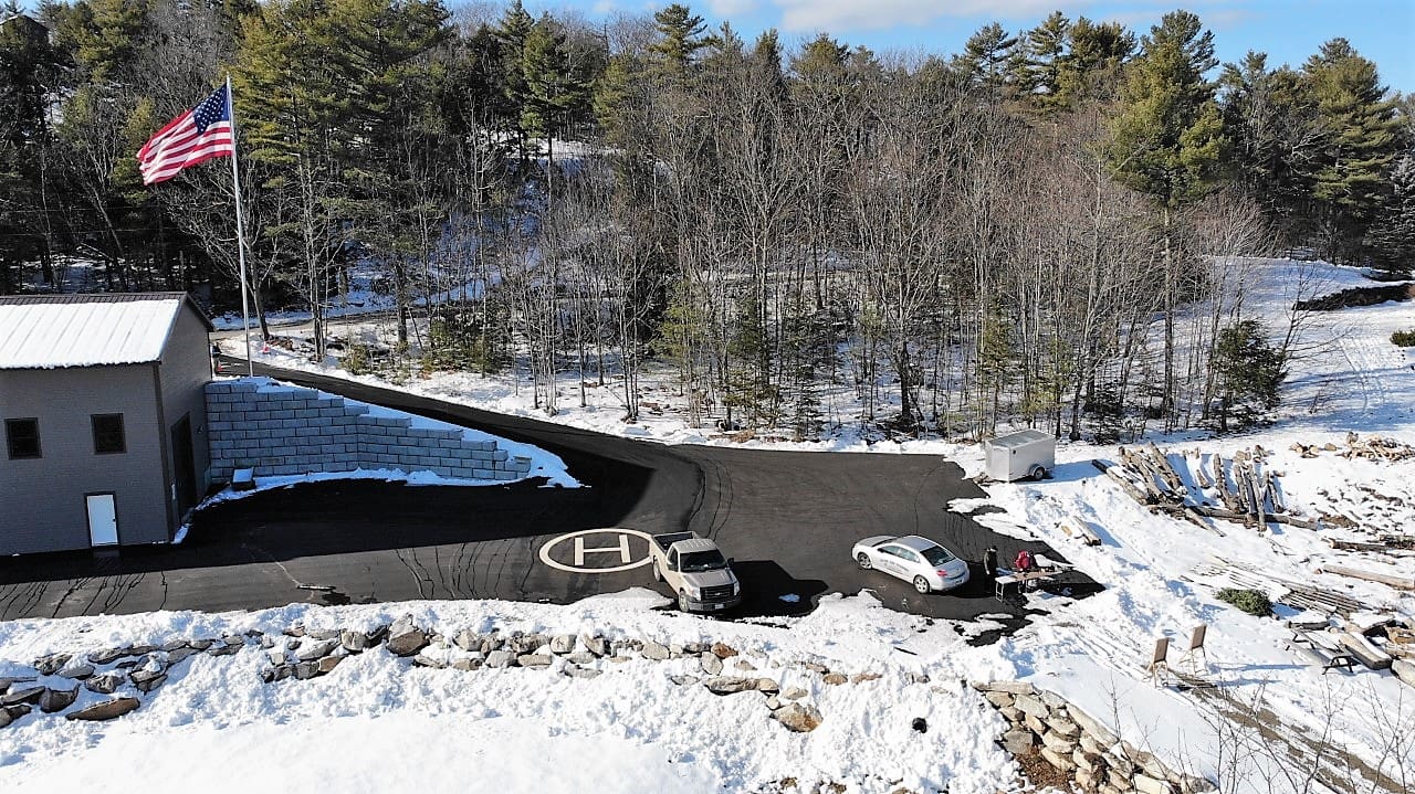 Snow-covered dam with water flowing through in a forested area.